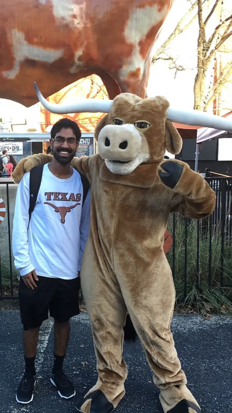 Vikas Peraka on the University of Texas at Austin campus, wearing a Texas shirt with an arm around the Longhorn mascot